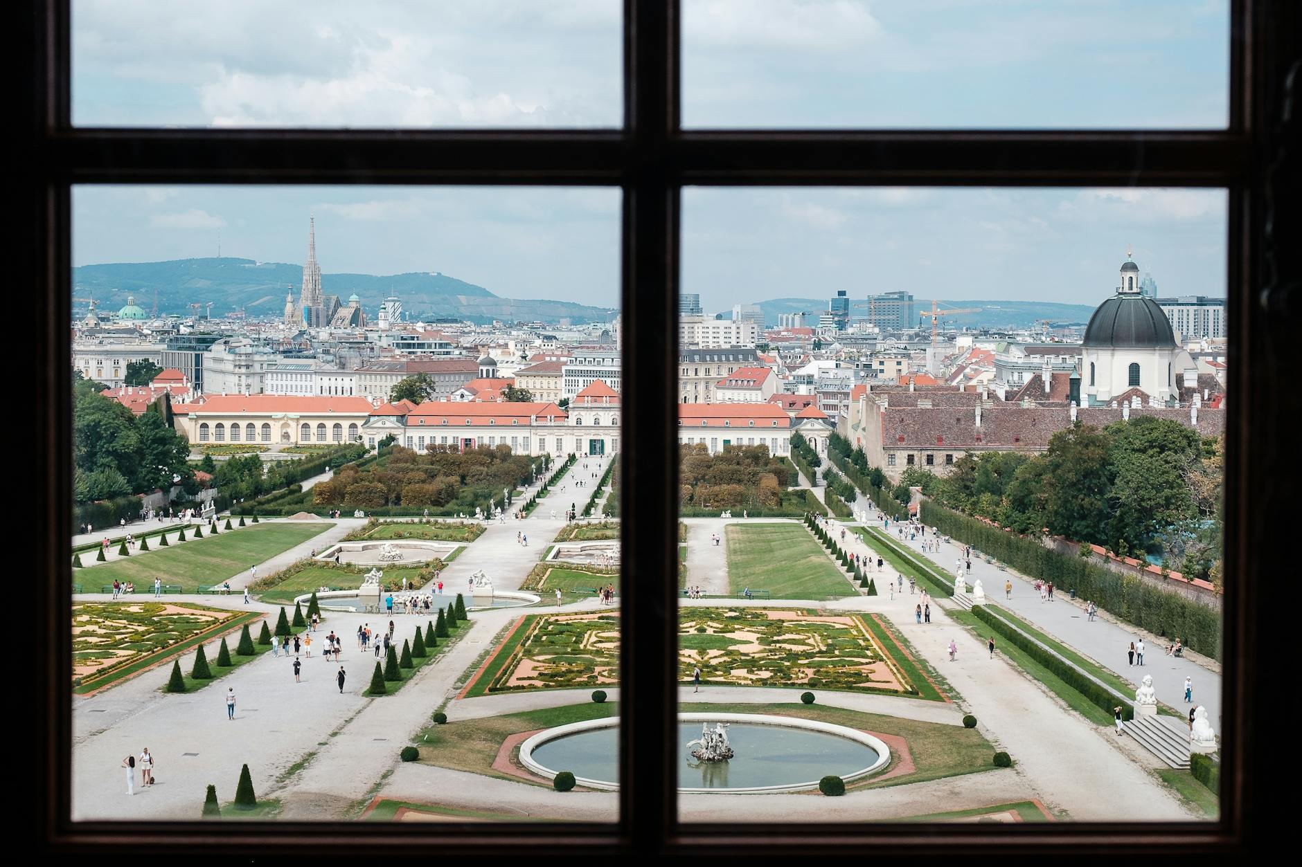 A breathtaking view of Vienna's Belvedere Palace gardens from a window, showcasing baroque architecture and urban landscape.